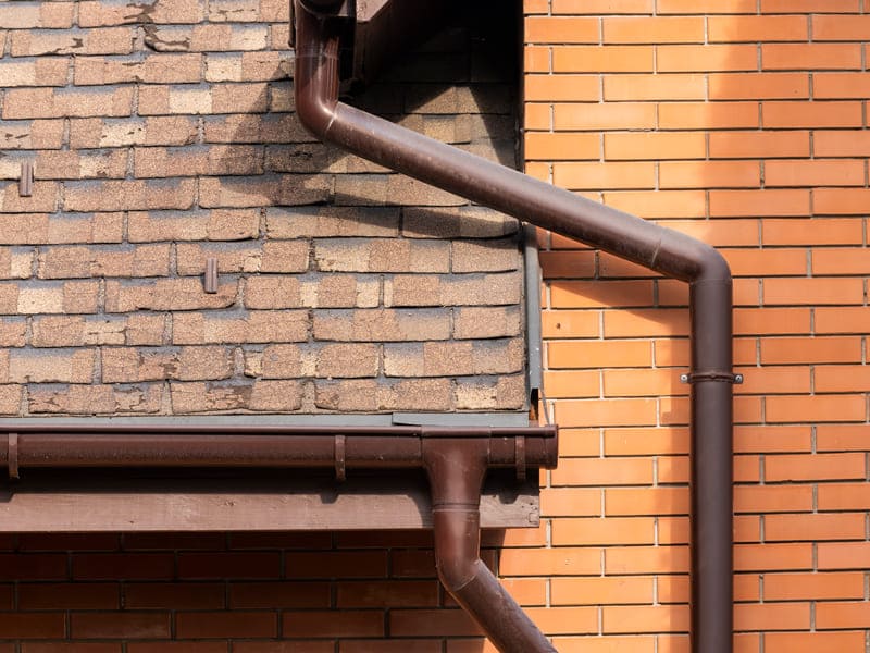 Brown pipe and gutter on a brick building, representing Quality Gutter Services in Manhattan, NY.